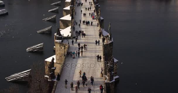 Туристы, идущие по Карлову мосту и далёкому Пражскому замку в солнечный день, Чехия. 4K наклон видео, вид сверху — стоковое видео