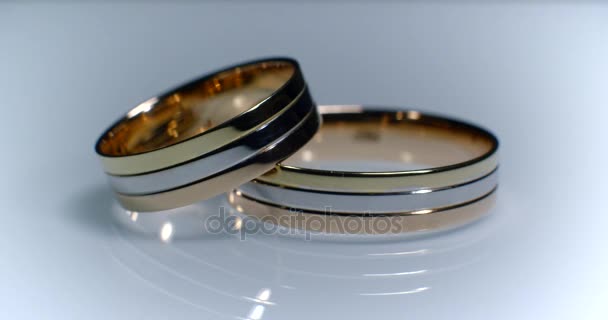 Twee Gouden trouwringen liggend op wit-grijs glanzend oppervlak met licht close-up macro. Transfusie van licht op ringen. — Stockvideo