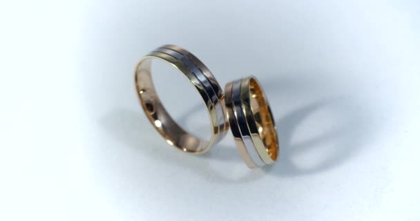 Two gold wedding rings lying on white-gray surface shining with light close up macro. Transfusion of light on rings. — Stock Video