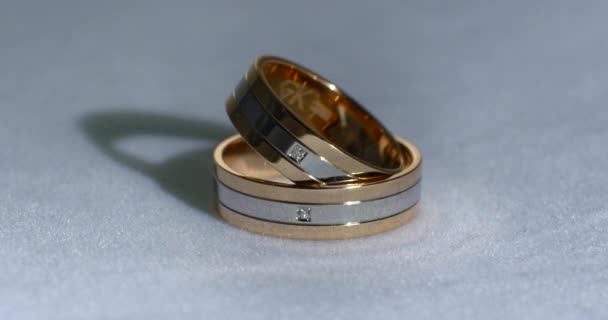 Due fedi nuziali in oro adagiate su una superficie bianco-grigia che brilla di luce macro ravvicinata. Trasfusione di luce sugli anelli . — Video Stock