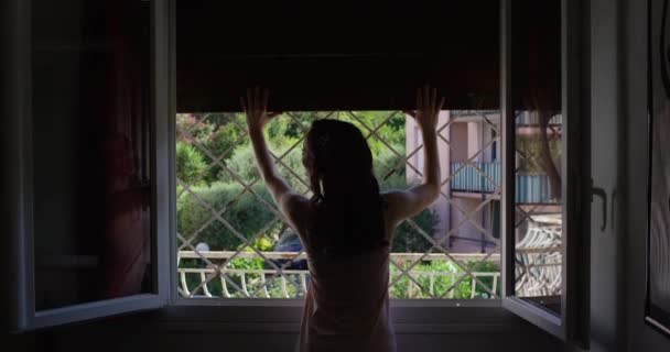 Atractiva joven abre ventana en cámara lenta y mirando al patio de pie cerca de la ventana en su casa y disfruta de la vista y las flores — Vídeos de Stock