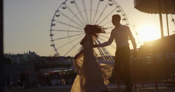 Pareja romántica besándose, bailando, volviéndose loca al atardecer en el parque cerca de Ferris Wheel, Niza, Francia. Disparo en cámara lenta 4k — Vídeos de Stock