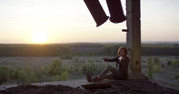 Tocando violino em prédio arruinado com pôr do sol 4K . — Vídeo de Stock