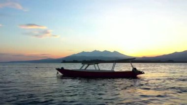 Arkasında bir tekne ve dağlarla okyanusun üzerinde güneşin doğuşunu gösteren drone görüntüsü. Endonezya, Gili Havayolları, 2020