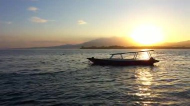 Arkasında bir tekne ve dağlarla okyanusun üzerinde güneşin doğuşunu gösteren drone görüntüsü. Endonezya, Gili Havayolları, 2020