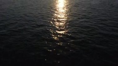 Okyanusun üzerindeki altın günbatımının ve ufuktaki dağların havadan görünüşü..