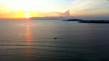 Okyanusun insansız hava aracı görüntüsü. Akıntılı bir balıkçı teknesiyle gün batımının üzerinde. Bir suya yansıyor..