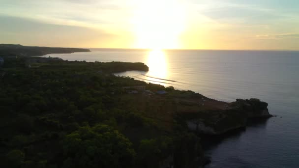 夕日の美しい海の水を背景に、山の崖の下の砂浜の空中ビュー。インドネシアのバリ. — ストック動画