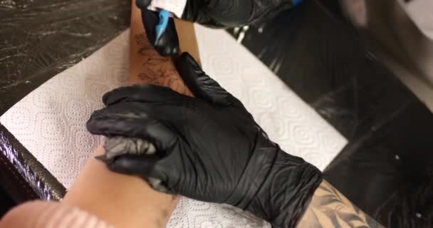 Close up tatuagem artista faz uma tatuagem em uma mão feminina com desenho de tinta de metralhadora . — Vídeo de Stock