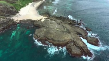 Deniz dalgalarının hava görüntüsü kayalara çarpıp çarpıyor. Okyanus dalgaları sıçrıyor ve köpük oluşturuyor..