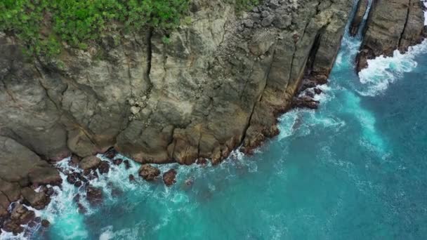 海の波がクラッシュし、岩の石を打つの空中ビュー。海の波が飛び散って泡を作る. — ストック動画