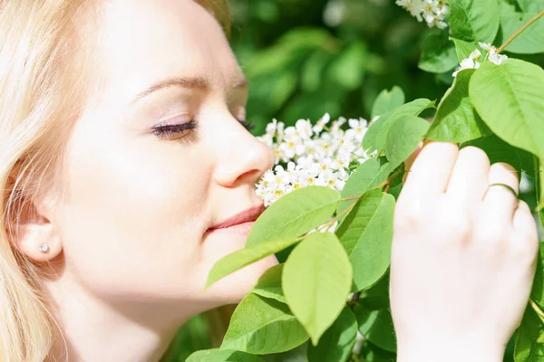 笑顔と緑の森で若い魅力的な白人女性は晴れた日を手で持ち、鳥の桜の花をスニッフィングします。 ストックフォト