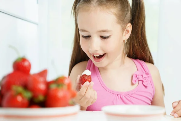 Joven linda sonriente niña europea está comiendo madura fresa jucy con crema agria y sosteniendo plato blanco de muchas bayas — Foto de Stock