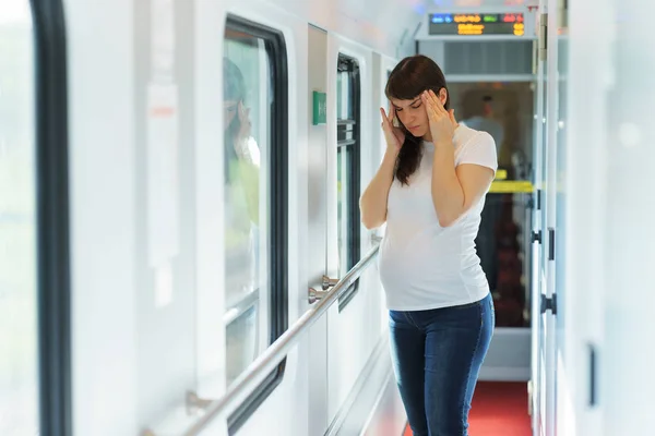 Una mujer embarazada europea en camiseta está teniendo dolor de cabeza mientras viaja en tren — Foto de Stock