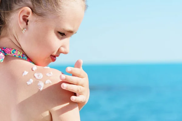 Jong meisje applyng zon beschermer crème op haar schouder op het strand dicht bij tropisch turkooizen zee onder de blauwe hemel — Stockfoto