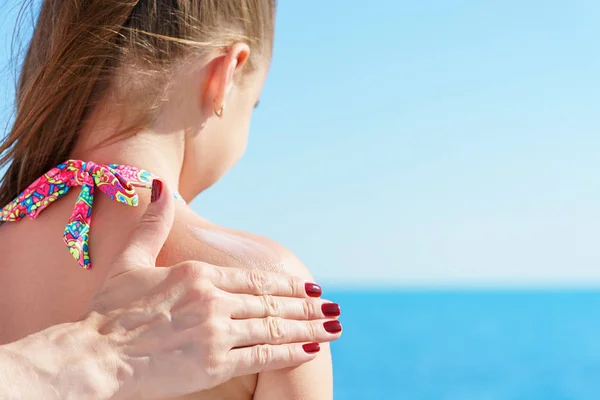 Maman eyropean appose crème protectrice solaire à l'épaule de sa jeune jolie fille sur la plage près de la mer tropicale turquoise sous le ciel bleu — Photo
