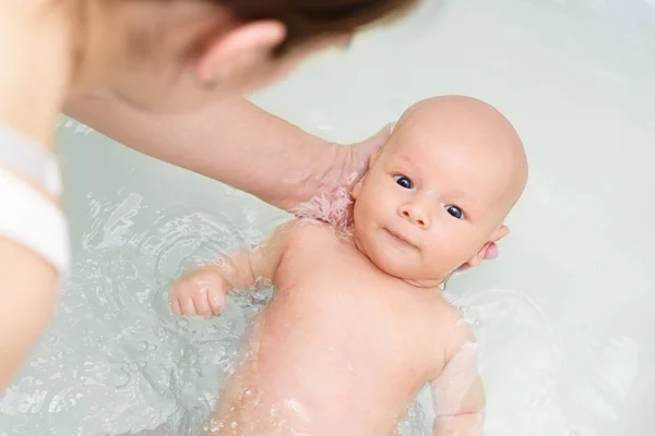 Beyaz kadın yeni doğan bebeği o banyo su üzerinde tutuyor