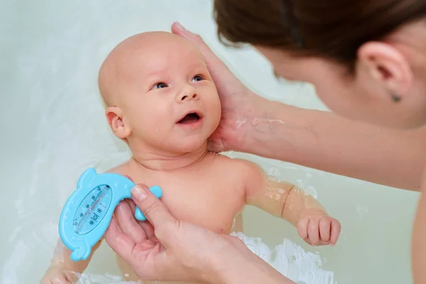 Beyaz kadın yeni doğan bebeği o banyo su üzerinde tutuyor