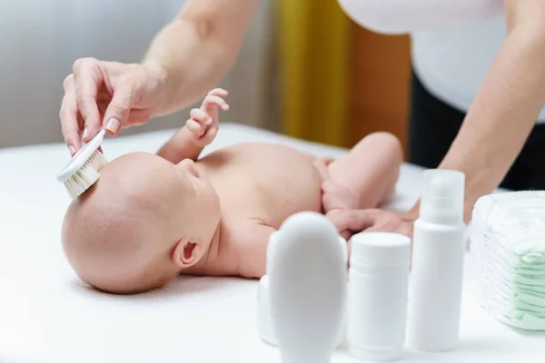 Mamá limpia la piel del bebé en la cabeza con un cepillo suave para el cuidado de la piel — Foto de Stock