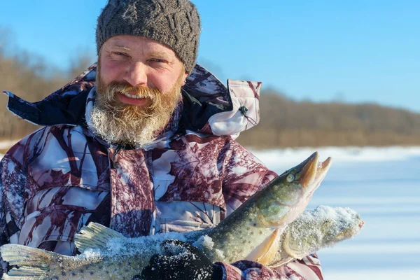 L'uomo barbuto sta tenendo pesce congelato dopo la pesca invernale di successo nella fredda giornata di sole — Foto Stock