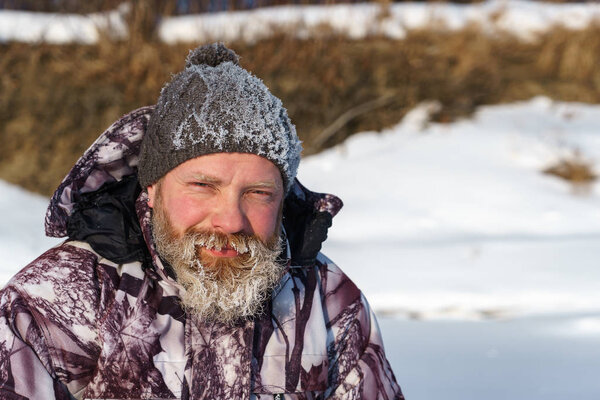 One euriopean bearded fisher man or hunter with ice and hoarfrost on beard is looking to the camera with smile