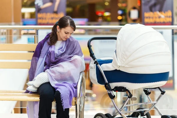 Menekşe çalmış olan Avrupa kadın küçük çocuğunu kapatmak için halka açık bir yerde alışveriş merkezi beyaz bebek arabası emzirme olduğunu