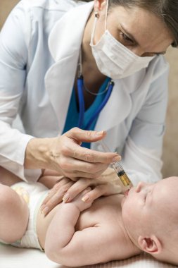 Bir beyaz kadın doktor sıvı ilaç bazı doz erkek bebek bebek şırınga tarafından ağız içine hastalık veya aşı randevu için veriyor.