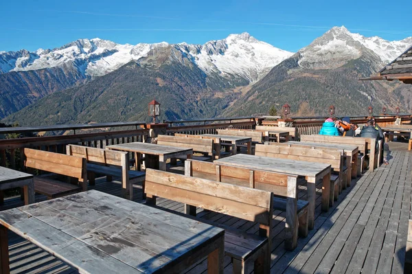Outdoor restaurant in the mountainsImage with the terrace of a , surrounded by the Alps mountains,  the rustic wooden tables ready to receive the guests.