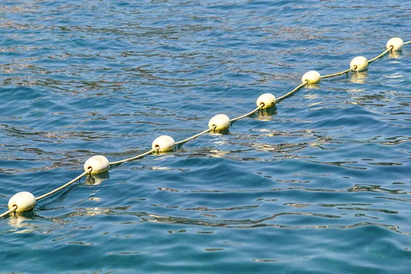 Line of yellow buoys against the blue sea. Restriction on open water. Glare and ripples on the water — Stock Photo, Image