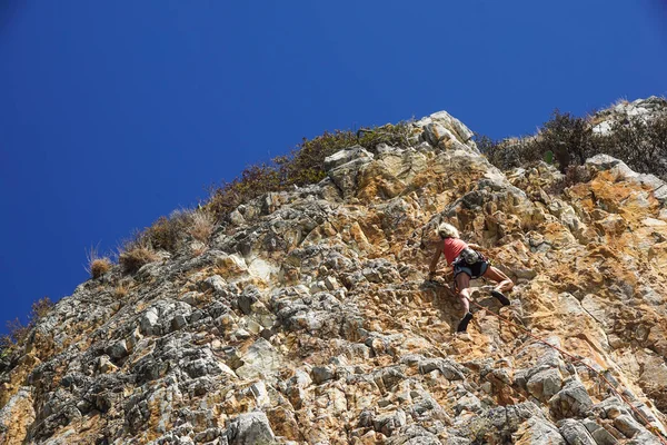 NAPLES, ITÁLIA - 04 de setembro de 2017: uma mulher não identificada e atlética sobe uma montanha perto do mar em um dia quente de verão.escalar o rosto da rocha é um esporte praticado por muitas pessoas — Fotografia de Stock