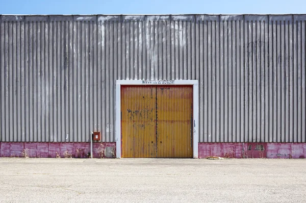 The sheet metal factory wall with the entrance door in the industrial park.The red door of the factory building.