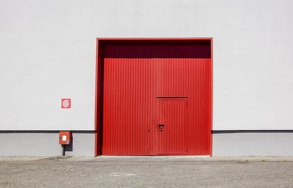 Le mur de l'usine de tôle avec la porte d'entrée rouge dans le parc industriel.La porte rouge du bâtiment de l'usine . — Photo