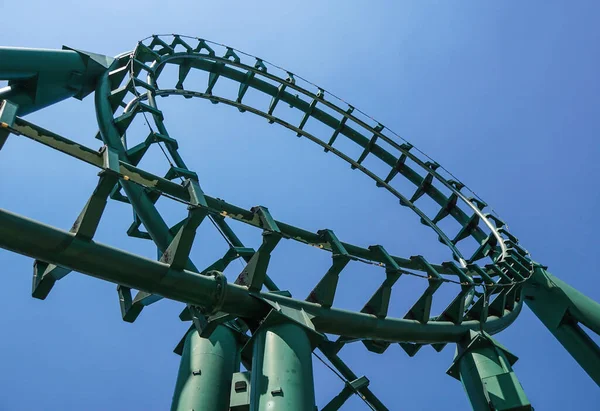 Rollercoaster curvo em um tema ou parque de diversões vazia faixas de metal verde e no fundo do céu azul. — Fotografia de Stock