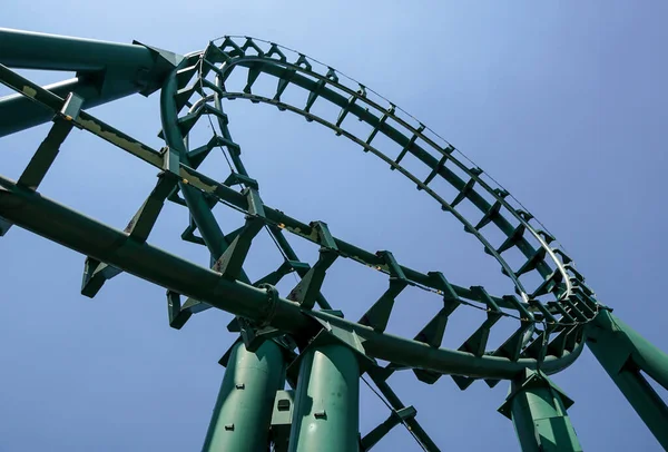 Rollercoaster curvo em um tema ou parque de diversões vazia faixas de metal verde e no fundo do céu azul. — Fotografia de Stock