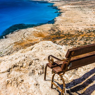 Bir bankta uçurumun kenarında oturan, Kıbrıs Adası'nın Akdeniz kıyısında pitoresk manzara gözlemleyebilirsiniz.