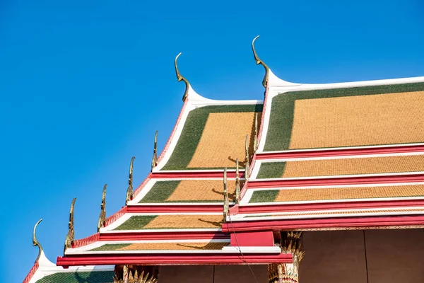 Multicolored sloping roofs of a Buddhist temple in the center of Bangkok against the blue sky.