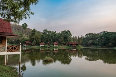 Güneşin ilk ışınları, Tayland 'ın orta kesimindeki orman boyunca akan Kwai nehri üzerindeki küçük evlerin çatılarını aydınlatır..