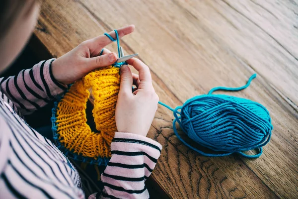 Young girl knitting a circle scarf with yellow and blue yarn