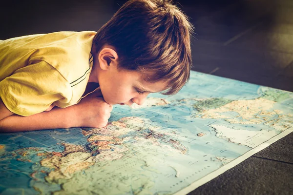 Young boy studying the world map. Dreaming of travel in the times of isolation.
