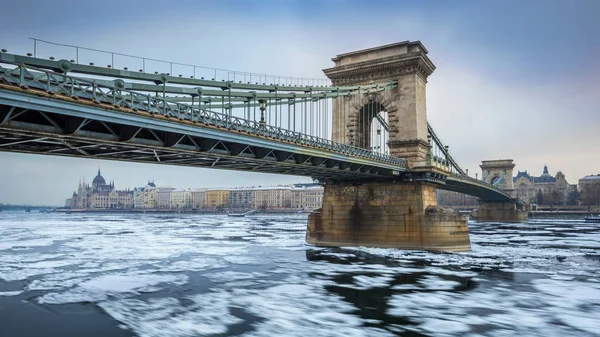 Budapest, Hongarije - de beroemde Szechenyi Chain Bridge op de ijzige rivier de Donau op een koude winterochtend met het Hongaarse Parlement op de achtergrond — Stockfoto
