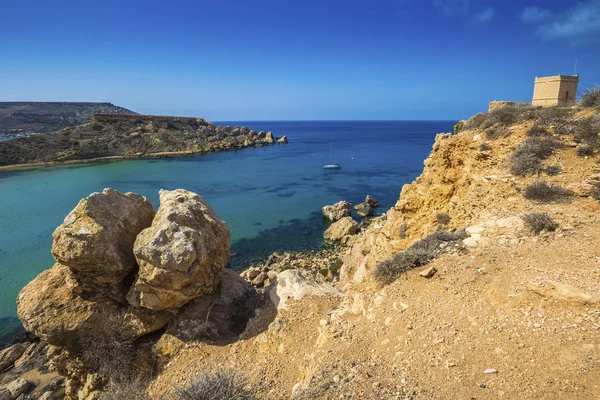 Malta - Enormes rocas y la torre Ghajn Tuffieha en un caluroso día de verano con agua azul cristalina del mar y barco de vela — Foto de Stock