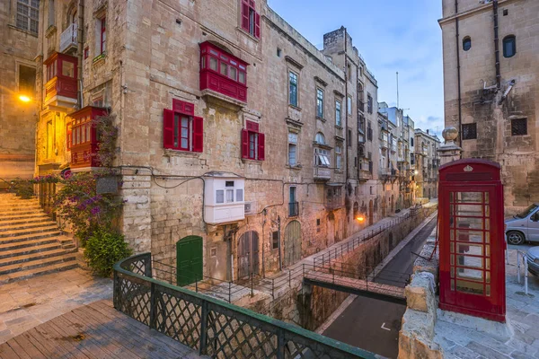 Valletta, Malta - röd vintage brittiska telefonhytt och gångbro och traditionella röda balkonger i den antika staden Valletta tidigt på morgonen — Stockfoto