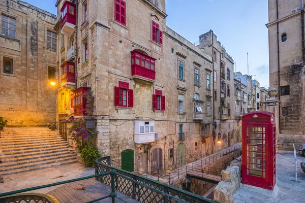 La Valeta, Malta - Red vintage británica cabina telefónica y pasarela y balcones rojos tradicionales en la antigua ciudad de La Valeta temprano en la mañana — Foto de Stock