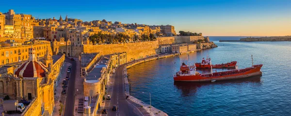 Valletta, Malta - panoramautsikt över stadssilhuetten i Valletta och Grand hamnen med vacker soluppgång, fartyg och klarblå himmel — Stockfoto