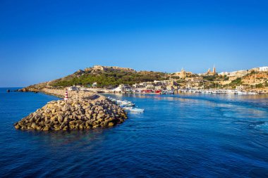 Gozo, Malta - The ancient port of Mgarr with lighthouse on the island of Gozo on a bright sunny summer day with blue sea water and clear sky clipart