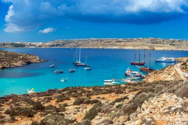 Comino, Malta - Panoramic skyline view of the famous and beautiful Blue Lagoon on the island of Comino with sailboats, traditional Luzzu boats and tourists enjoying the azure mediterranean sea water and sunshine clipart