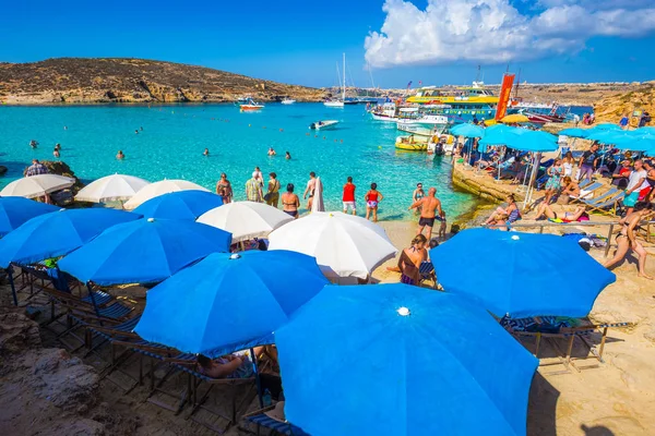 블루 라군, 코 미노, 몰타-10 월 18 일, 2016: 관광객 군중을 코 미노 섬, 몰타와 Gozo의 섬 배경에서 2016 년 10 월 18 일 화창한 날에 우산 아래 맑은 청록색 물을 즐길 수. — 스톡 사진
