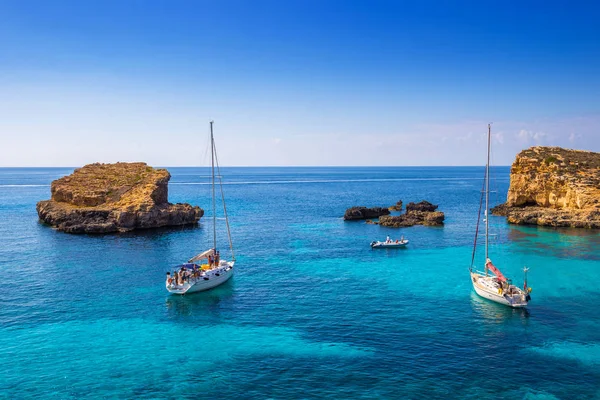 Comino, Malta - segelbåtar på den vackra blå lagunen på Comino Island med turkos klart havsvatten, blå himmel och stenar i vattnet — Stockfoto
