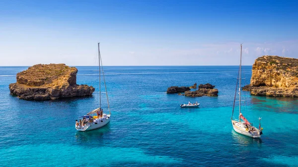 Comino, Malta - vitorlások, a gyönyörű Blue Lagoon, Comino-sziget türkiz tiszta tengervíz, a kék ég és a sziklák a vízbe — Stock Fotó