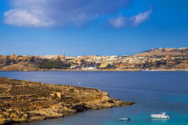 Comino Malta - motorówka i jacht o słynnej Błękitnej Laguny na wyspę Comino z Gozo i Mgarr miasto w tle na jasny słoneczny letni dzień — Zdjęcie stockowe